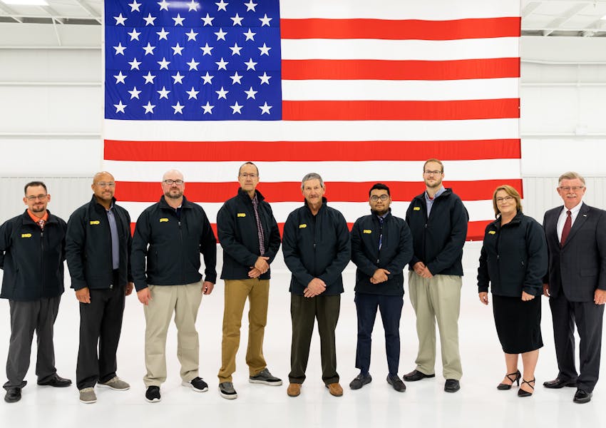 A group of DMP University trainees stand in front of a large American flag.